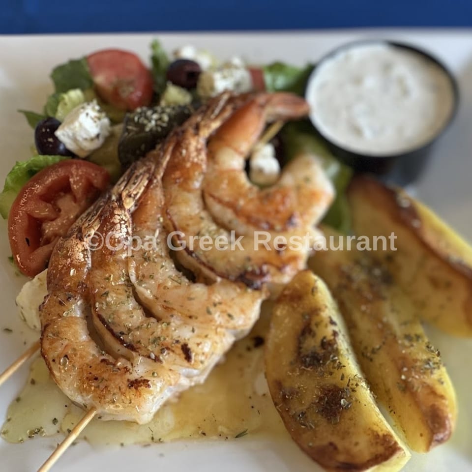 Grilled shrimp skewers with Greek salad, potato wedges, and tzatziki sauce from Opa Greek Restaurant.