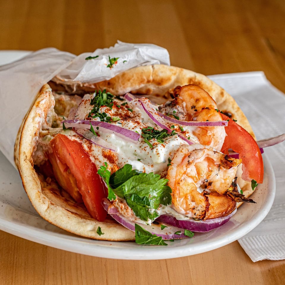 A Greek shrimp pita with tomatoes, red onions, tzatziki, and parsley on a white plate.