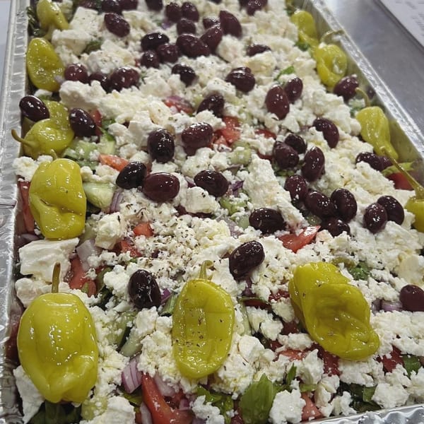 A large tray of Greek salad with feta cheese, Kalamata olives, and pepperoncini.