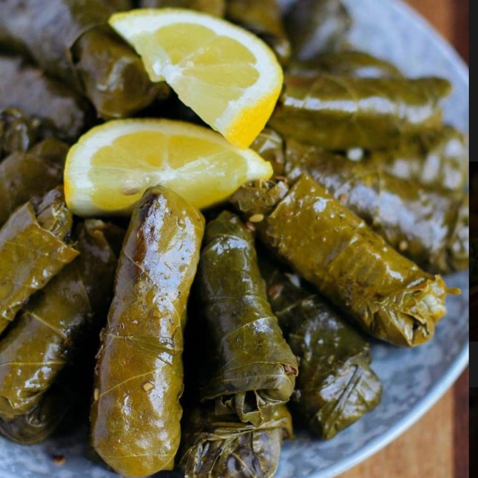 A close-up of Opa Greek Restaurant's dolmades, grape leaves stuffed with rice, garnished with lemon wedges.