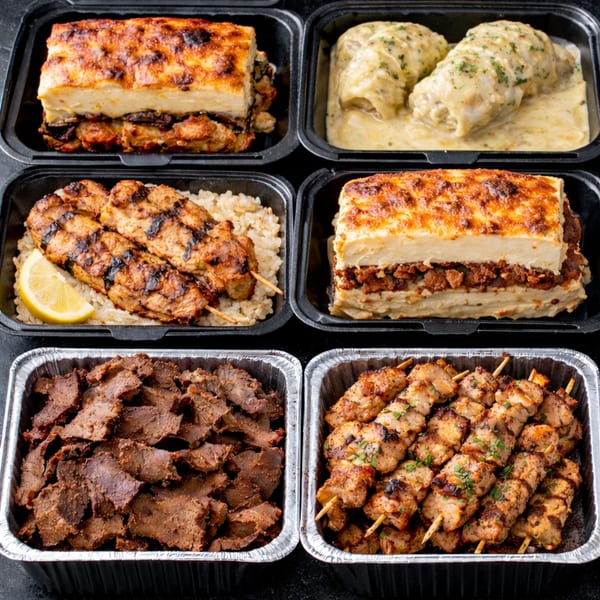 Six containers of Greek food, including moussaka, stuffed cabbage, chicken skewers, and gyro meat.