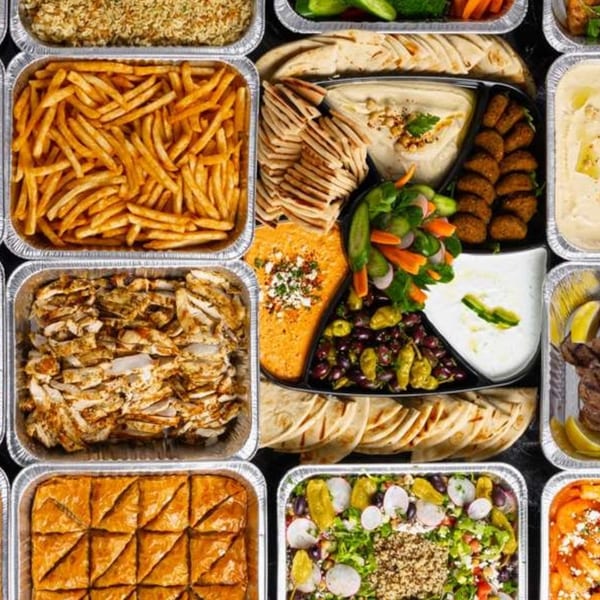 Assortment of Mediterranean catering dishes, including hummus, pita, falafel, chicken, fries, and baklava.