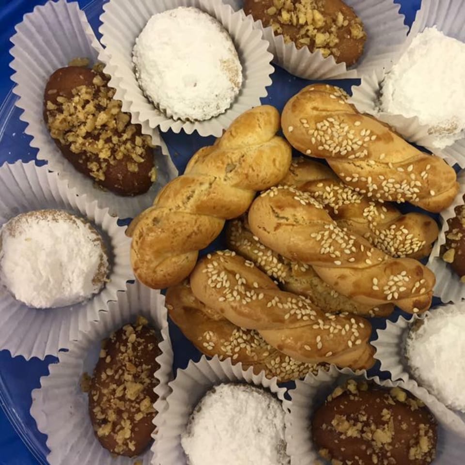Assortment of Greek pastries, including twisted sesame cookies, powdered sugar cookies, and nut-topped pastries.